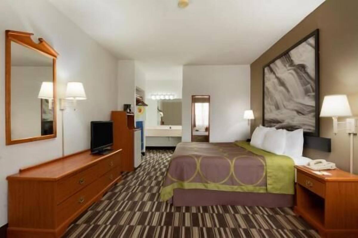 Habitación de hotel con cama, televisor, cómoda, espejo y un cuadro en la pared.