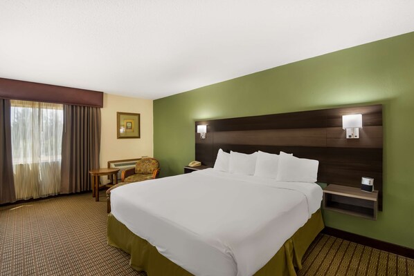 A hotel room with a large bed, a nightstand, a chair, a desk, and a picture on the wall.