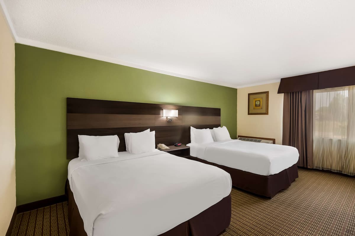 A hotel room with two beds, a headboard with a light fixture, a bedside table with a phone, and a window with curtains.