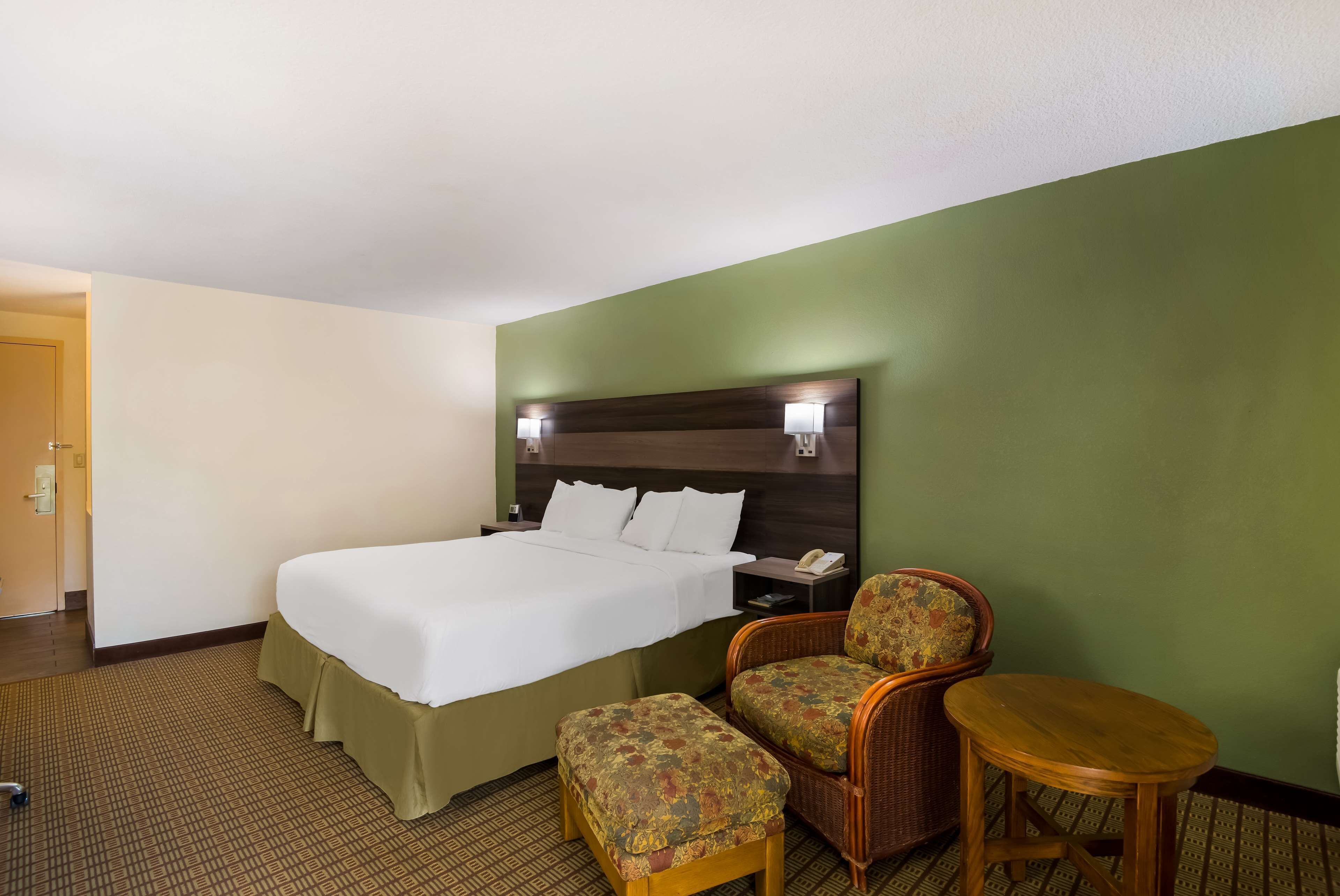 A hotel room with a large bed, two chairs, a small table, and a nightstand with a phone.