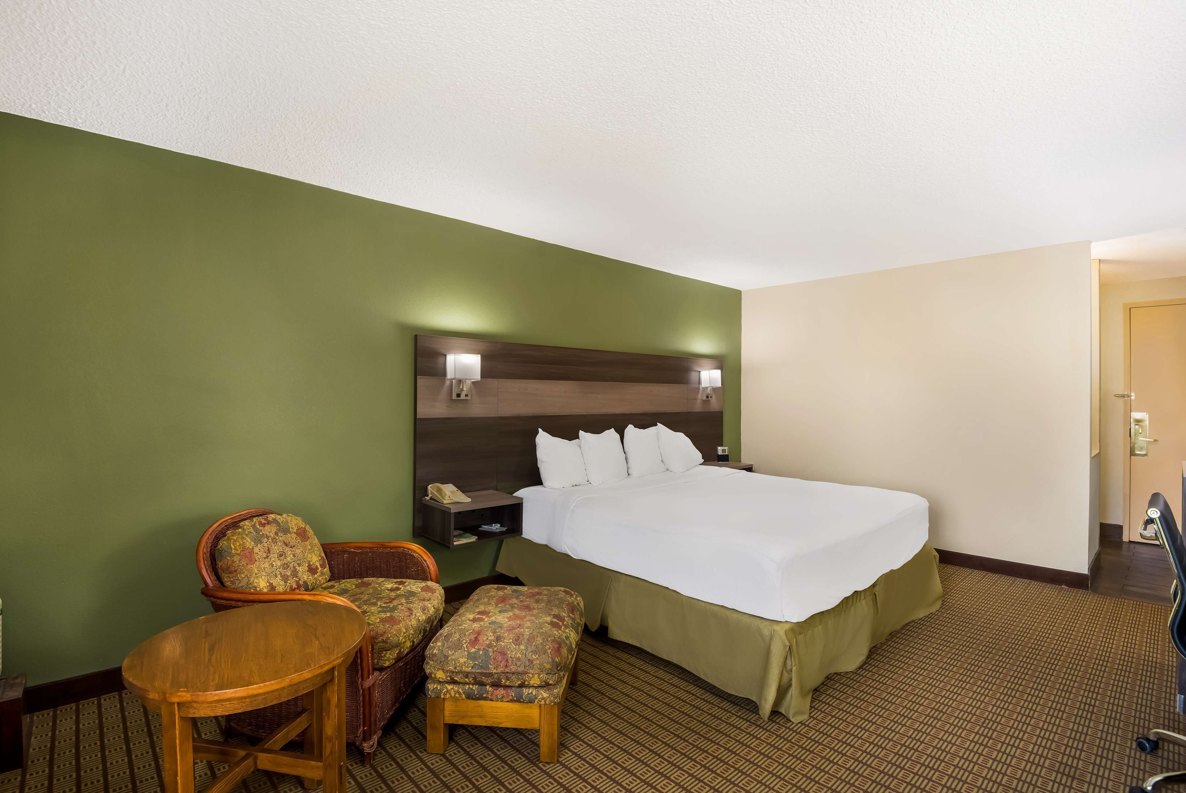 Hotelkamer met een bed, een stoel, een klein tafeltje en een nachtkastje met een lamp.