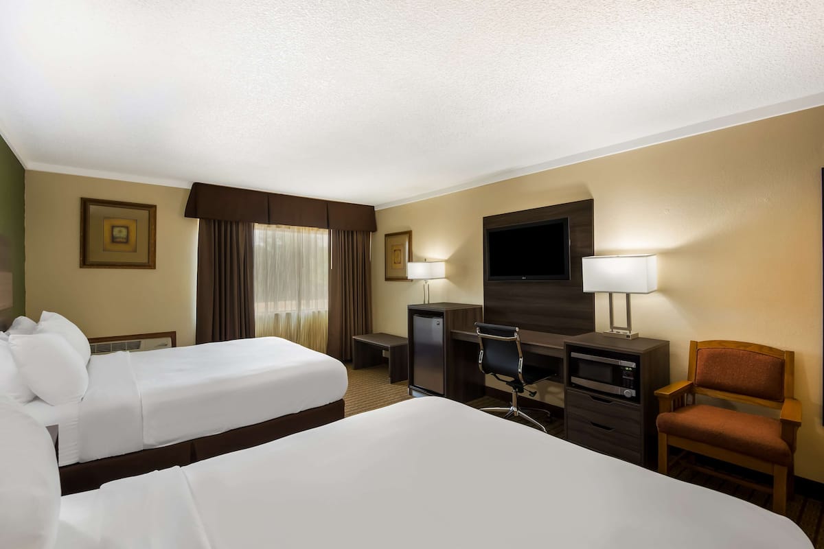 A hotel room with two beds, a desk, a chair, a TV, and a minibar.
