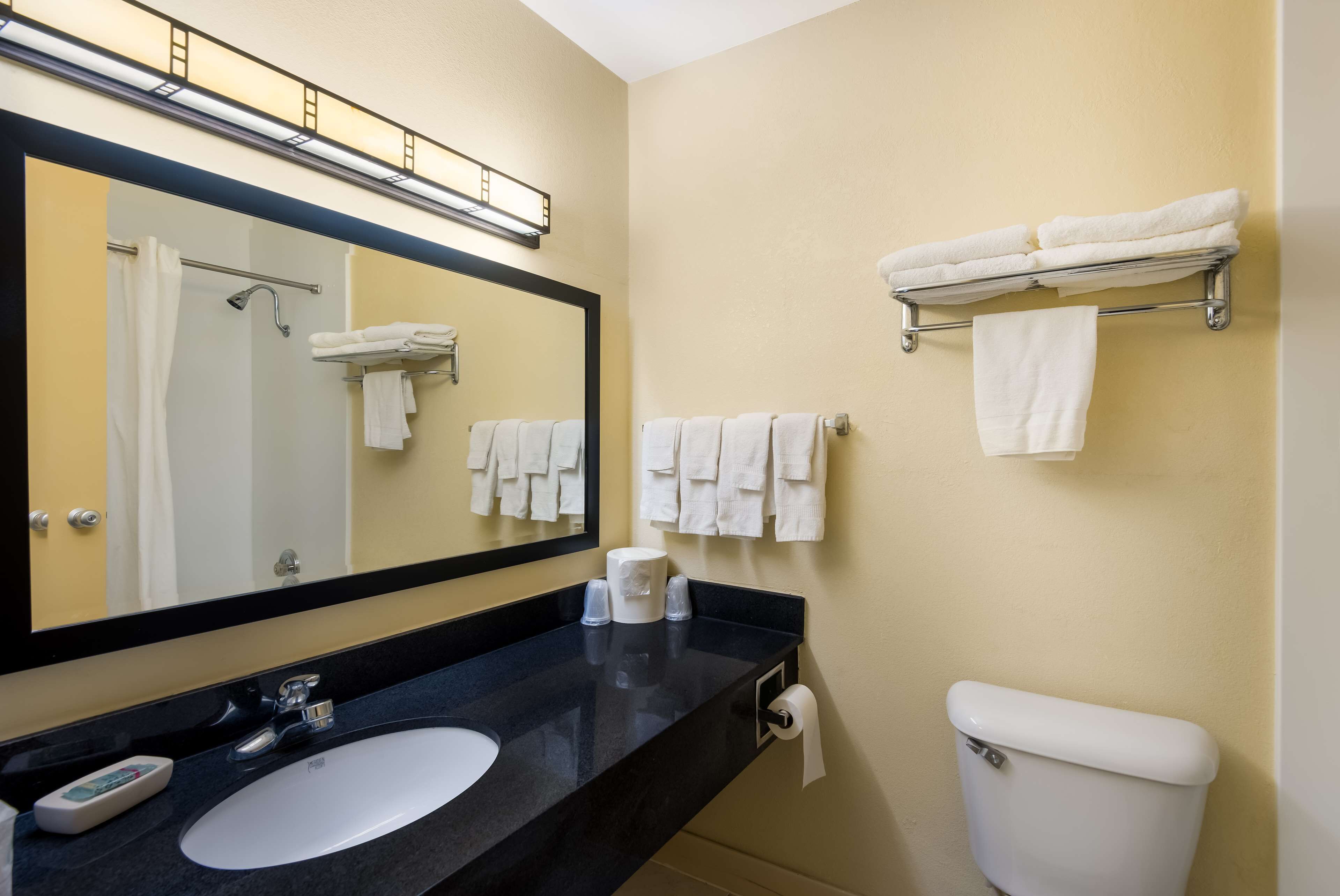 A bathroom with a black countertop, white sink, and a toilet. There are towels hanging on a rack and a mirror above the sink.