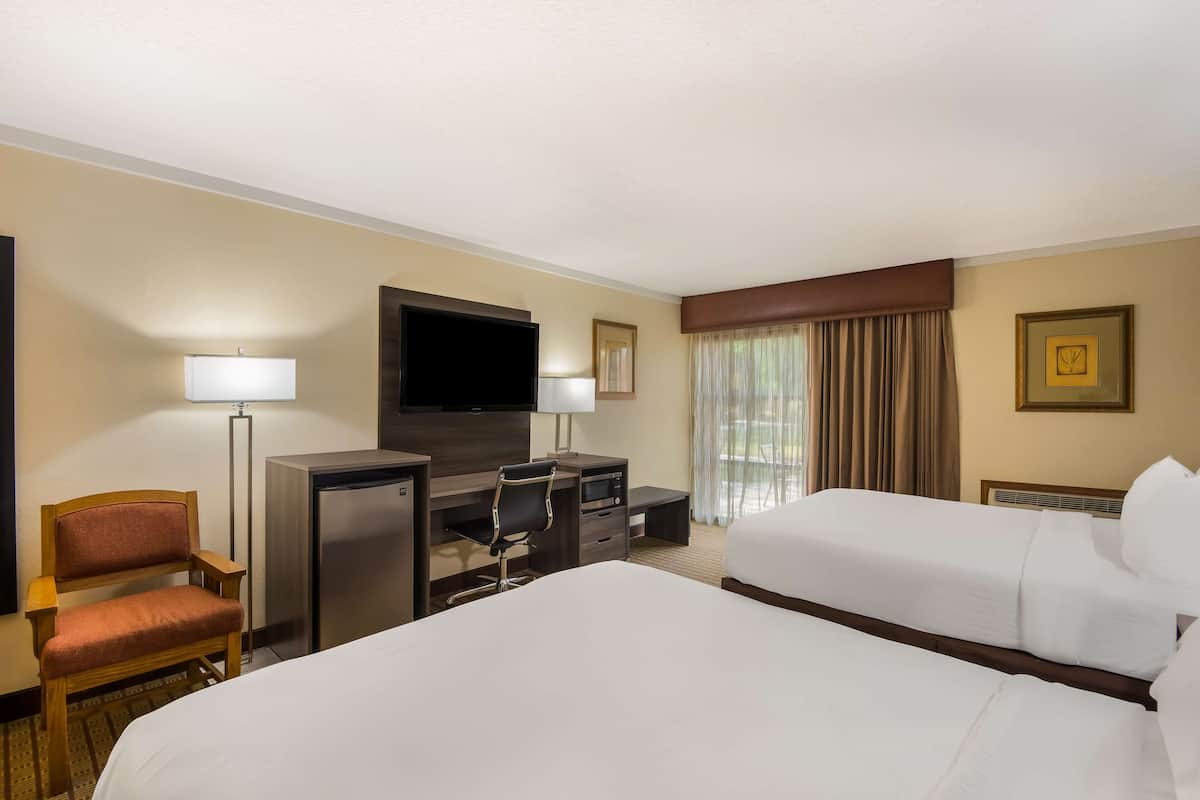 A hotel room with two beds, a desk, a chair, a television, and a window with curtains.