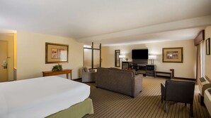 Quarto de hotel com uma cama grande, um sofá, uma escrivaninha com televisão de tela plana e uma mesinha de cabeceira com abajur.