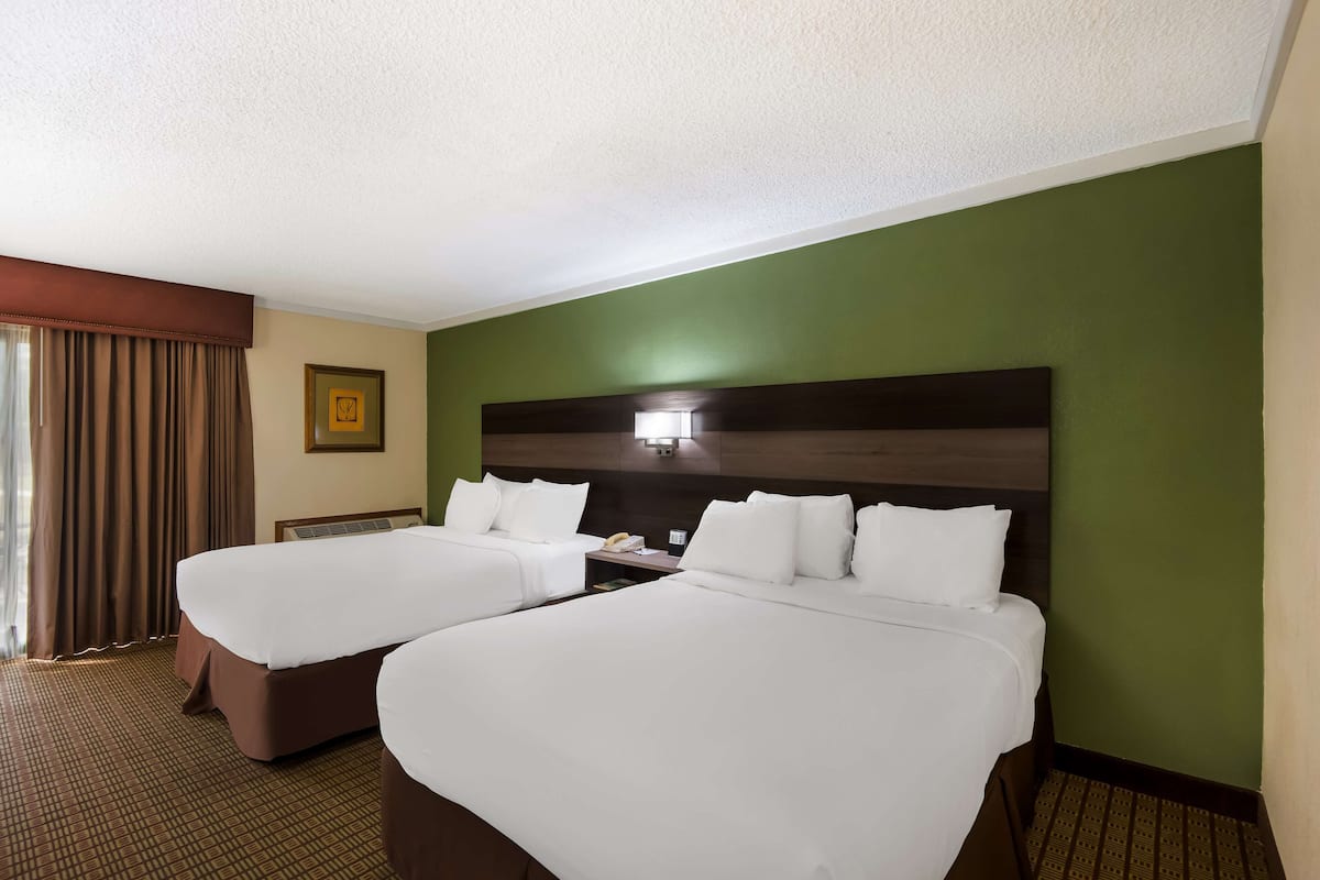A hotel room with two beds, a nightstand, a lamp, and a framed picture on the wall.