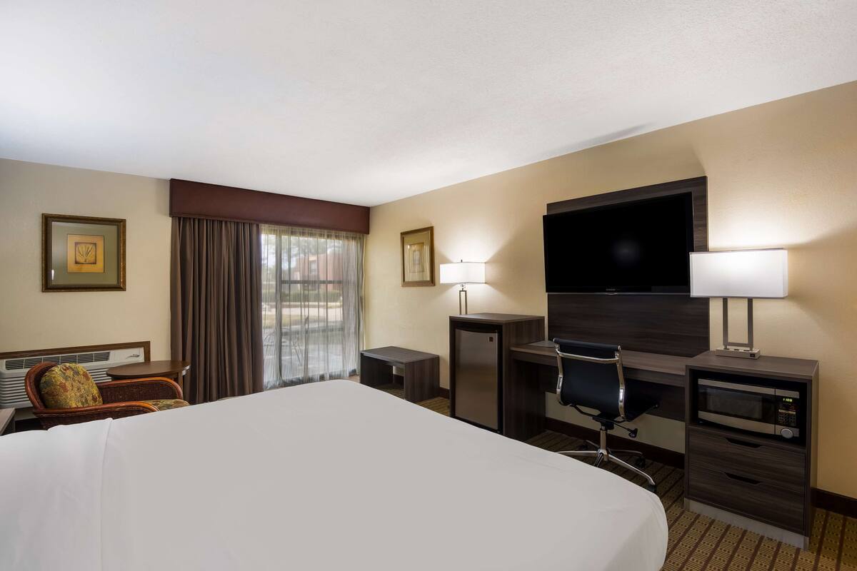 A hotel room with a large bed, a desk with a computer, a TV, a chair, and a small table.