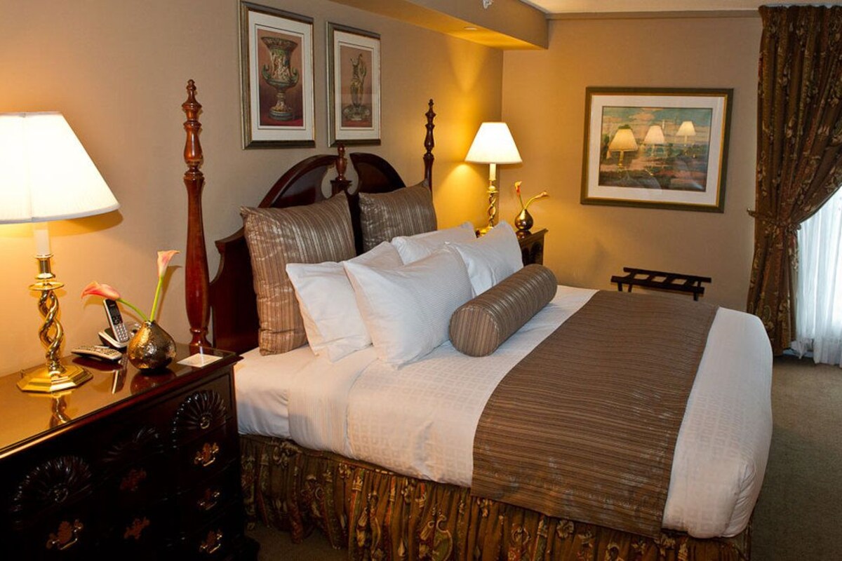 Quarto de hotel com cama grande, duas luminárias de cabeceira, penteadeira com espelho, TV de tela plana na parede e janela com cortinas.