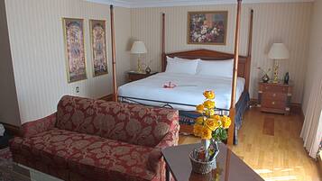 A hotel room with a four-poster bed, a red patterned sofa, a wooden coffee table with a vase of yellow flowers, and a small table with a lamp.