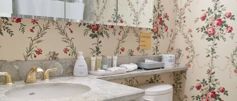 A bathroom with a marble sink, gold faucets, a white toilet, and floral wallpaper.