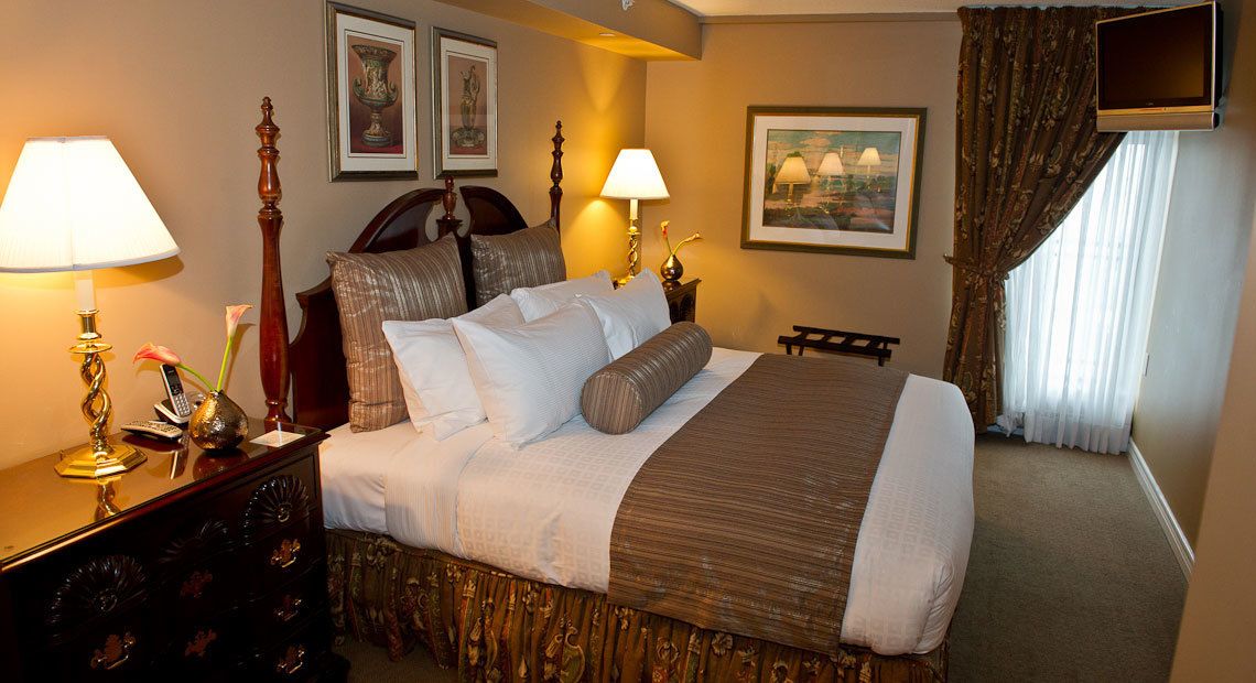 A hotel room with a large bed, two bedside tables with lamps, a dresser, and a TV mounted on the wall.