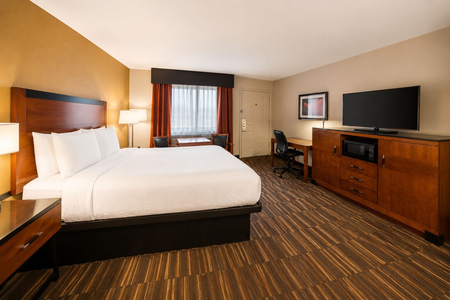 A hotel room with a large bed, a desk, a chair, a television, and a microwave.