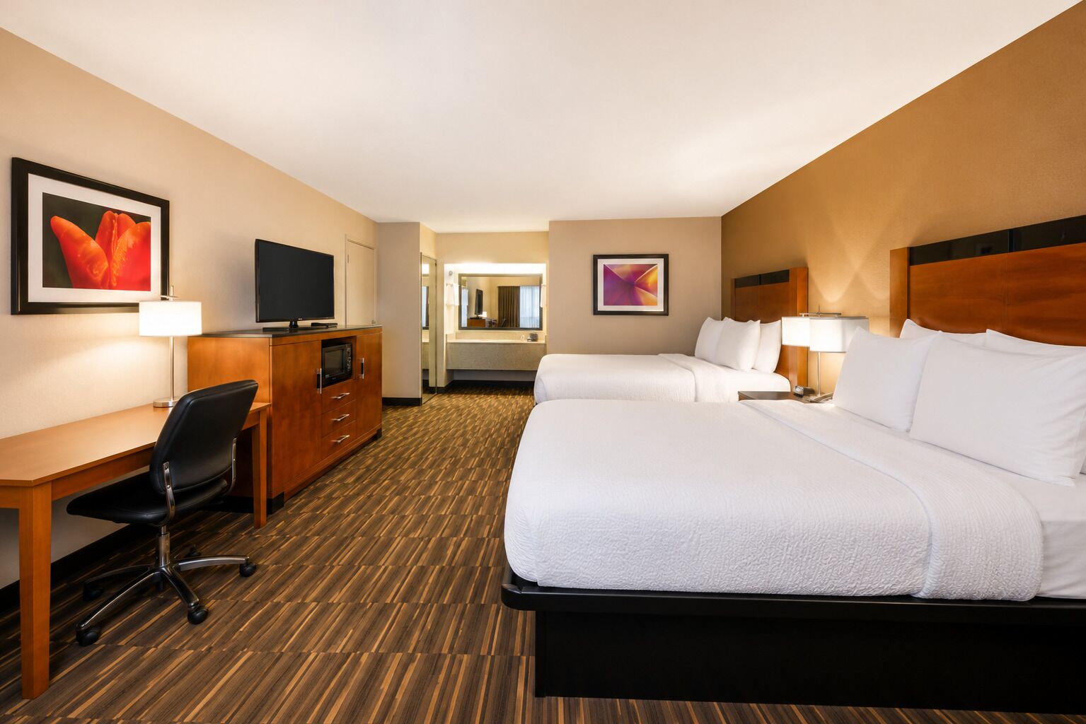 A hotel room with a large bed, a desk with a chair, a TV, and a dresser.
