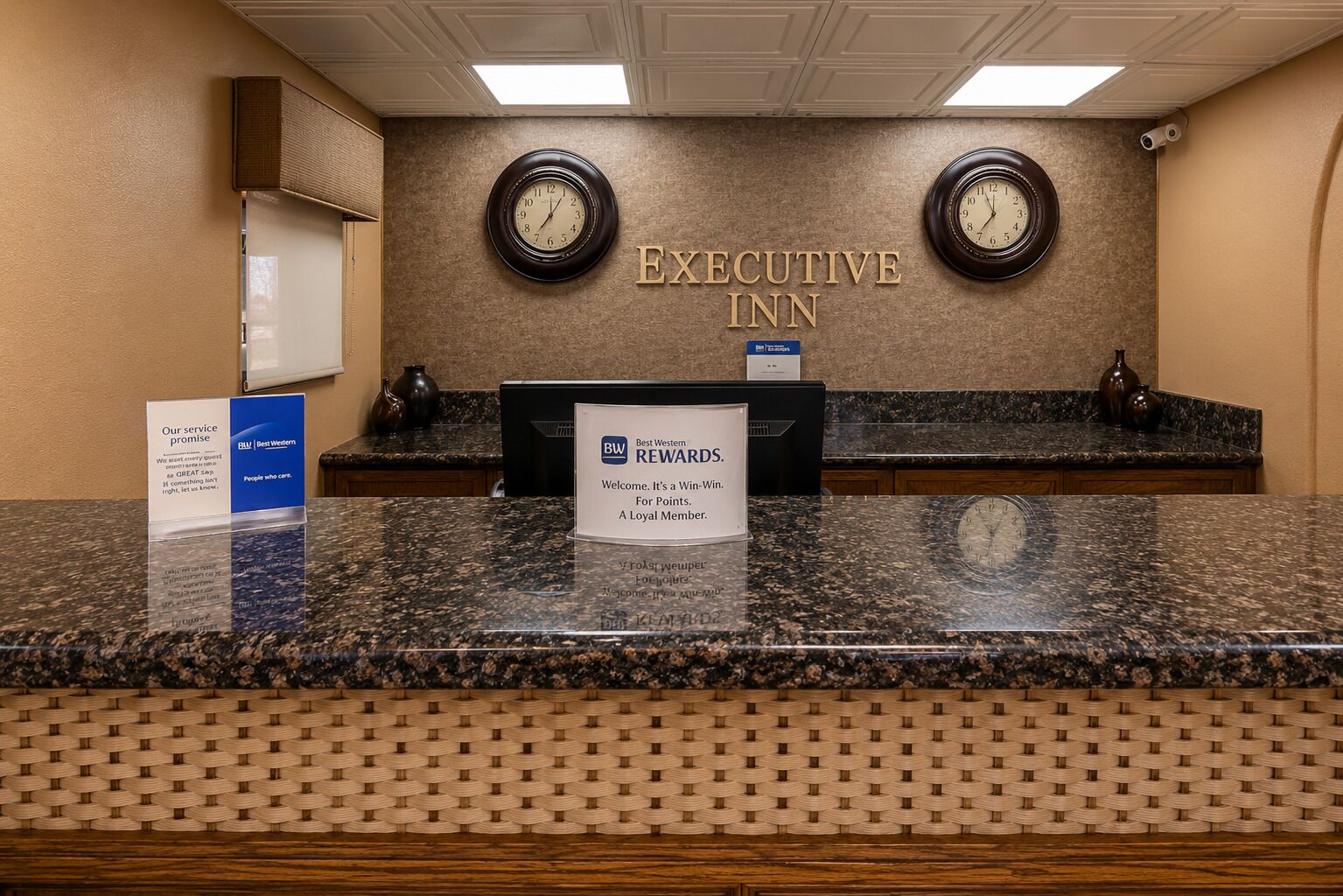 A reception desk with a sign reading 'EXECUTIVE INN' and two clocks above it.