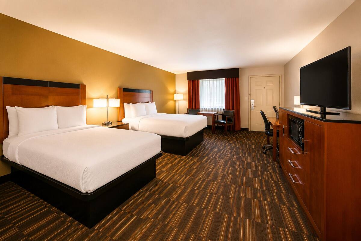 A hotel room with two beds, a desk, a chair, a television, and a minibar.