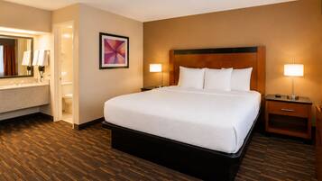 A hotel room with a large bed, a bathroom with a shower, a bedside table with a lamp, and a wall-mounted picture.