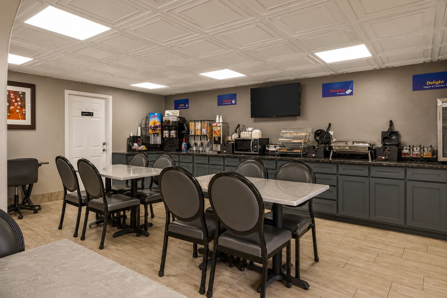 Un comedor con mesas y sillas, una estación de café y un televisor de pantalla plana en la pared.