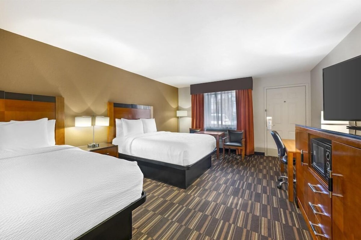 A hotel room with two beds, a desk, a chair, a television, and a large window with curtains.
