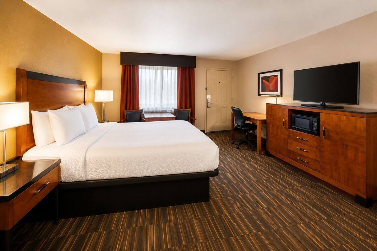 A hotel room with a large bed, a desk with a chair, a television, and a microwave.