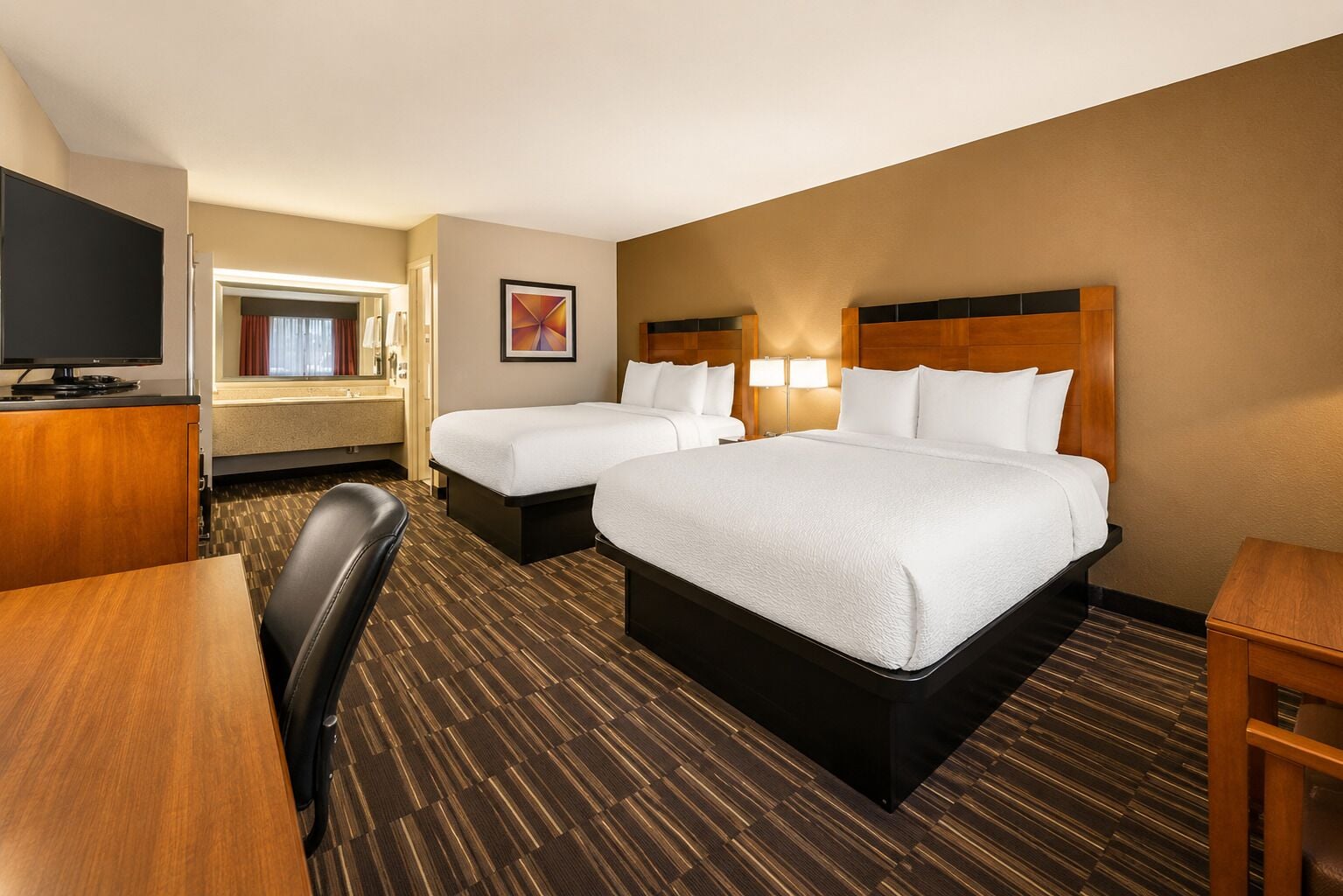 A hotel room with two beds, a desk, a television, and a bathroom visible through an open door.