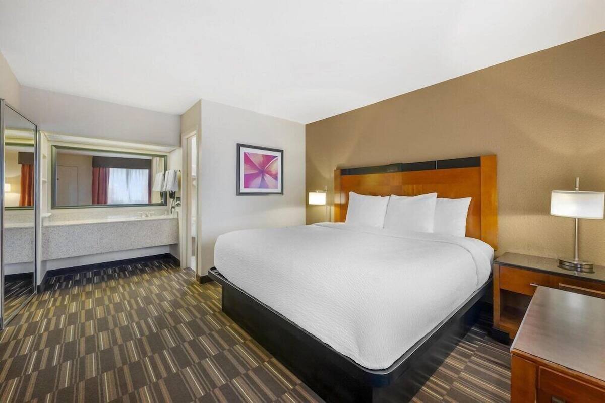 A hotel room with a large bed, a bedside table, a nightstand, a mirror, and a framed picture on the wall.