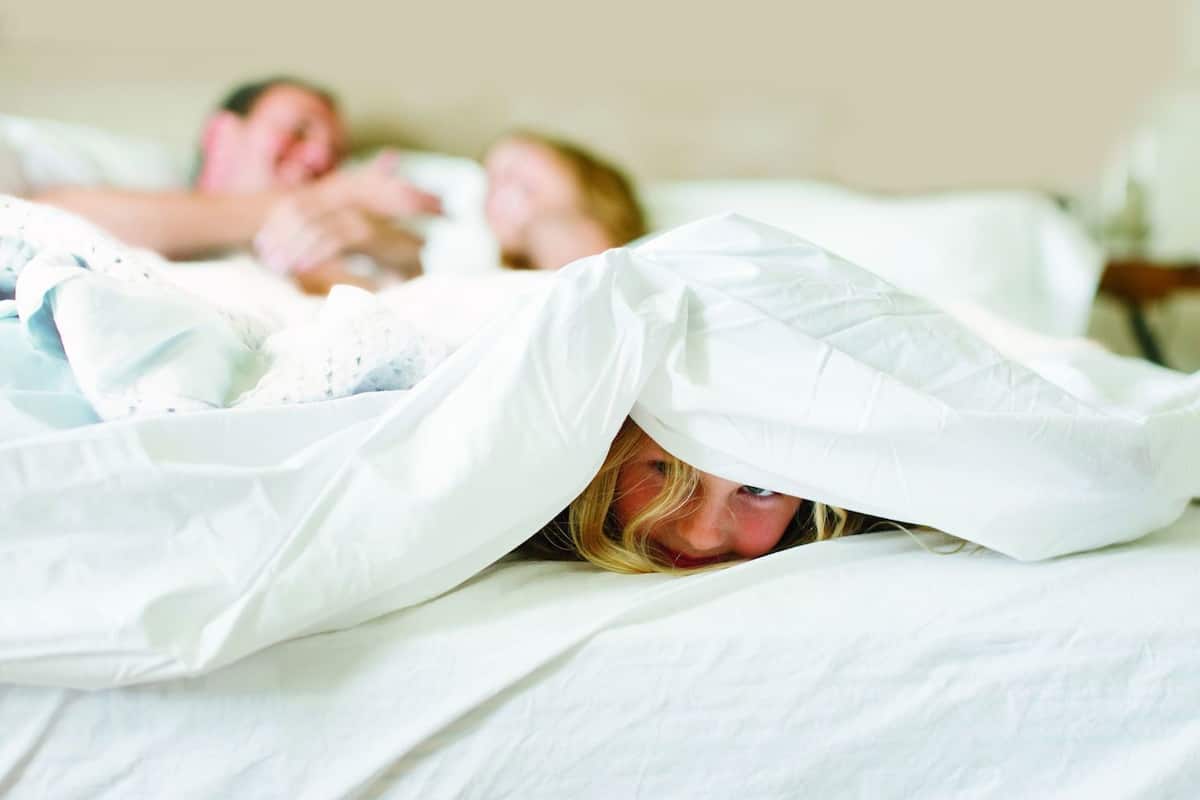 A bed with white bedding and a person partially covered by a white blanket.