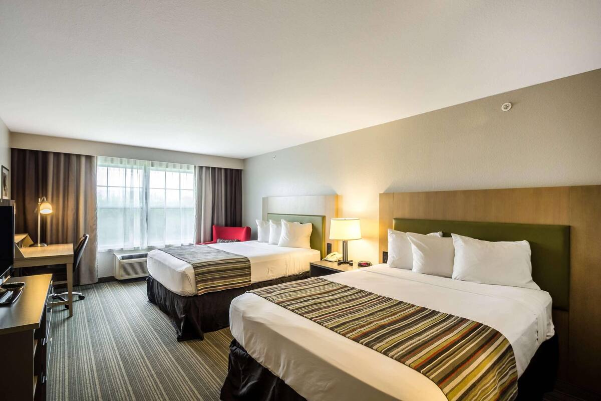 A hotel room with two beds, a desk, a chair, a TV, and a window with curtains.