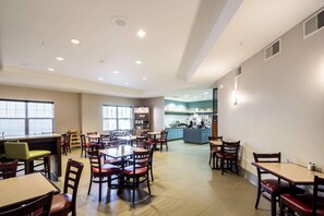 A spacious restaurant with multiple dining tables and chairs, a kitchen area in the background, and large windows providing natural light. - Country Inn & Suites by Radisson, Fond du Lac, WI (Fond du Lac)