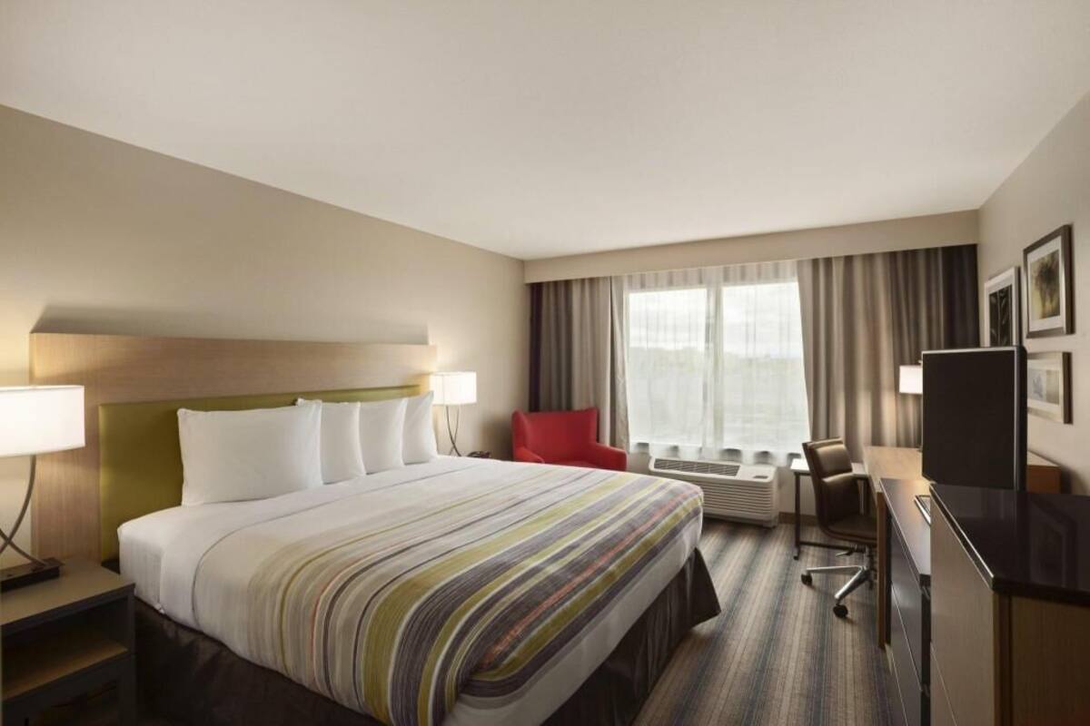 A hotel room with a bed, a desk, a chair, a TV, and a window with curtains.