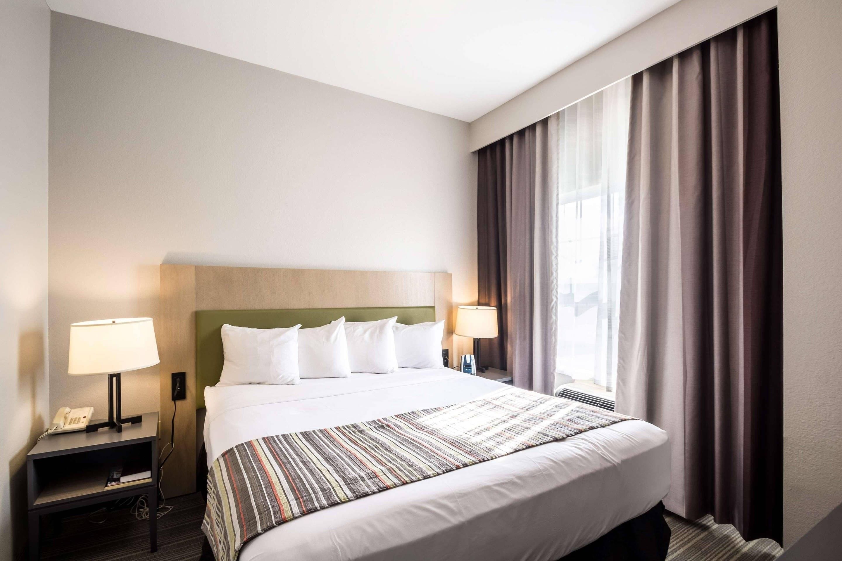 Habitación de hotel con cama, dos lámparas de noche, un teléfono, una ventana con cortinas y cabecero.