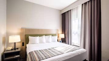 Habitación de hotel con cama, dos lámparas de noche, un teléfono, una ventana con cortinas y cabecero.
