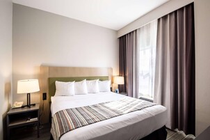 Habitación de hotel con cama, dos lámparas de noche, un teléfono, una ventana con cortinas y cabecero.