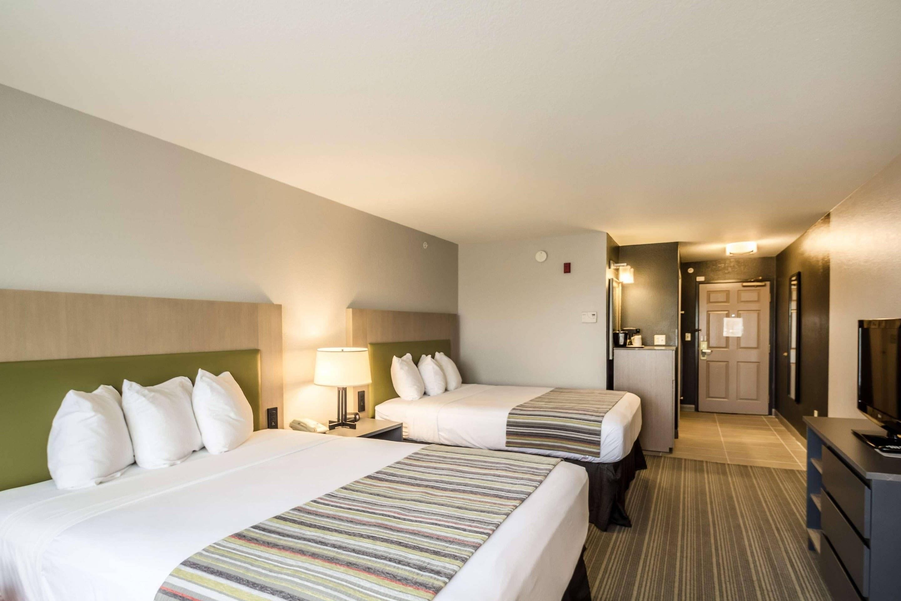 Une chambre d’hôtel avec deux lits, un bureau, une chaise, une télévision et une porte donnant sur un couloir.