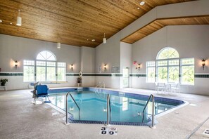Una amplia piscina interior con techo de madera, ventanas de vidrio transparente y piso de baldosas azules.