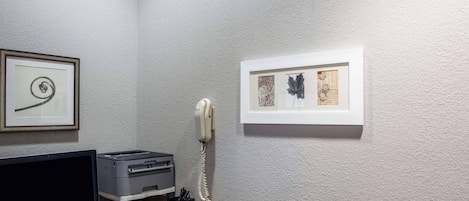 Ein Zimmer mit Schreibtisch, Desktop-Computer, Drucker, Telefon und gerahmten Bildern an der Wand.