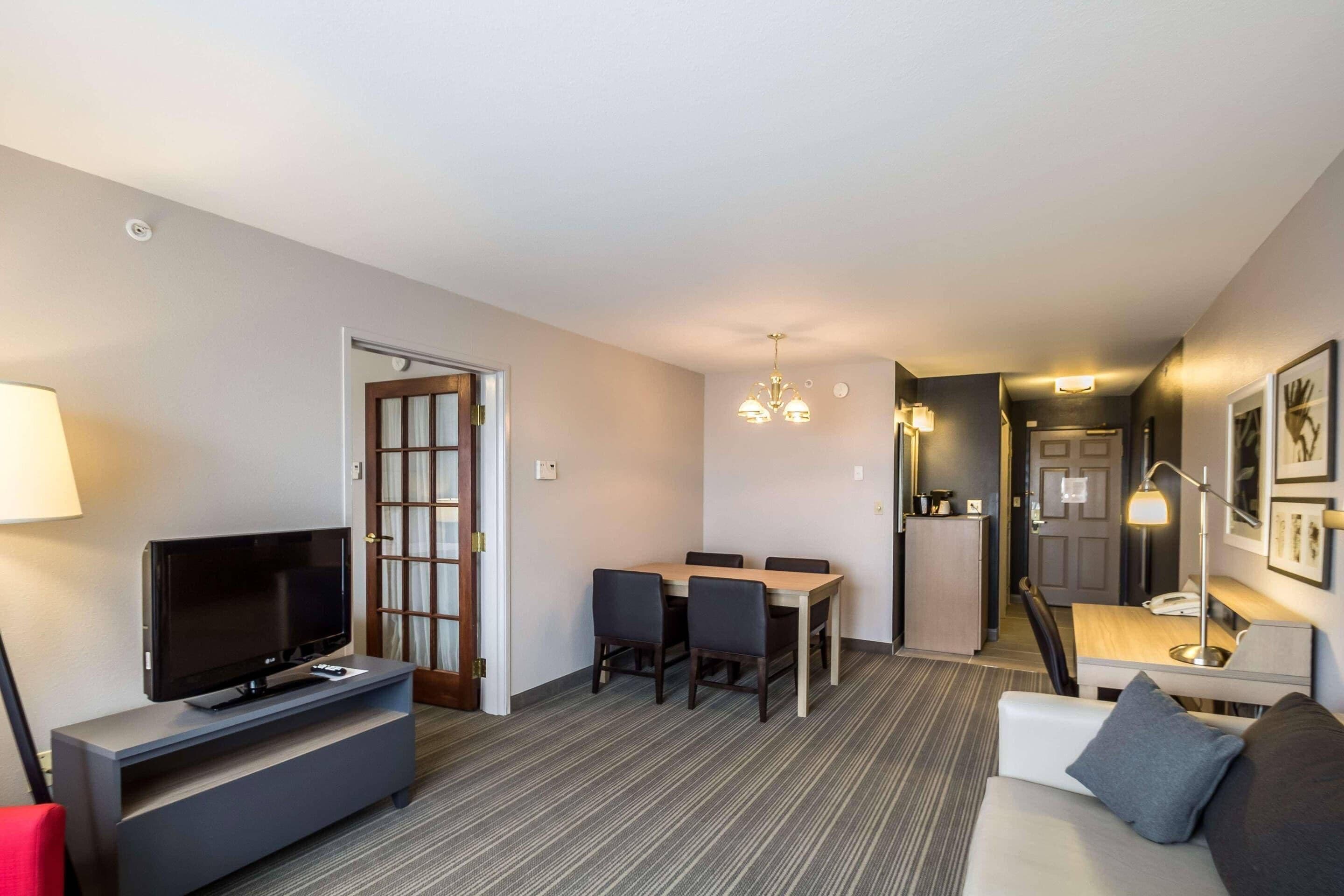Une chambre d’hôtel équipée d’une télévision, d’une table à manger, de chaises, d’un canapé, d’une lampe et d’un bureau avec un téléphone.