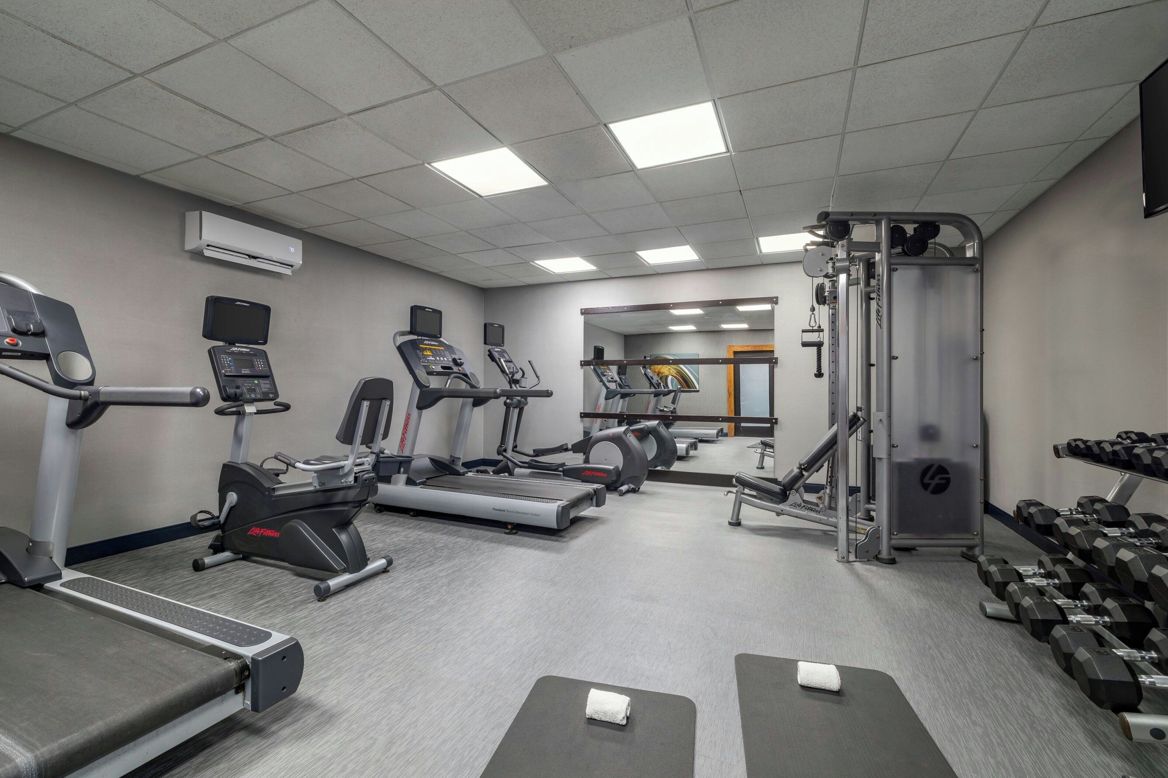Un gimnasio con cintas de correr, elípticas, una banca de pesas y una jaula para sentadillas.