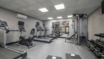 Un gimnasio con cintas de correr, elípticas, una banca de pesas y una jaula para sentadillas.