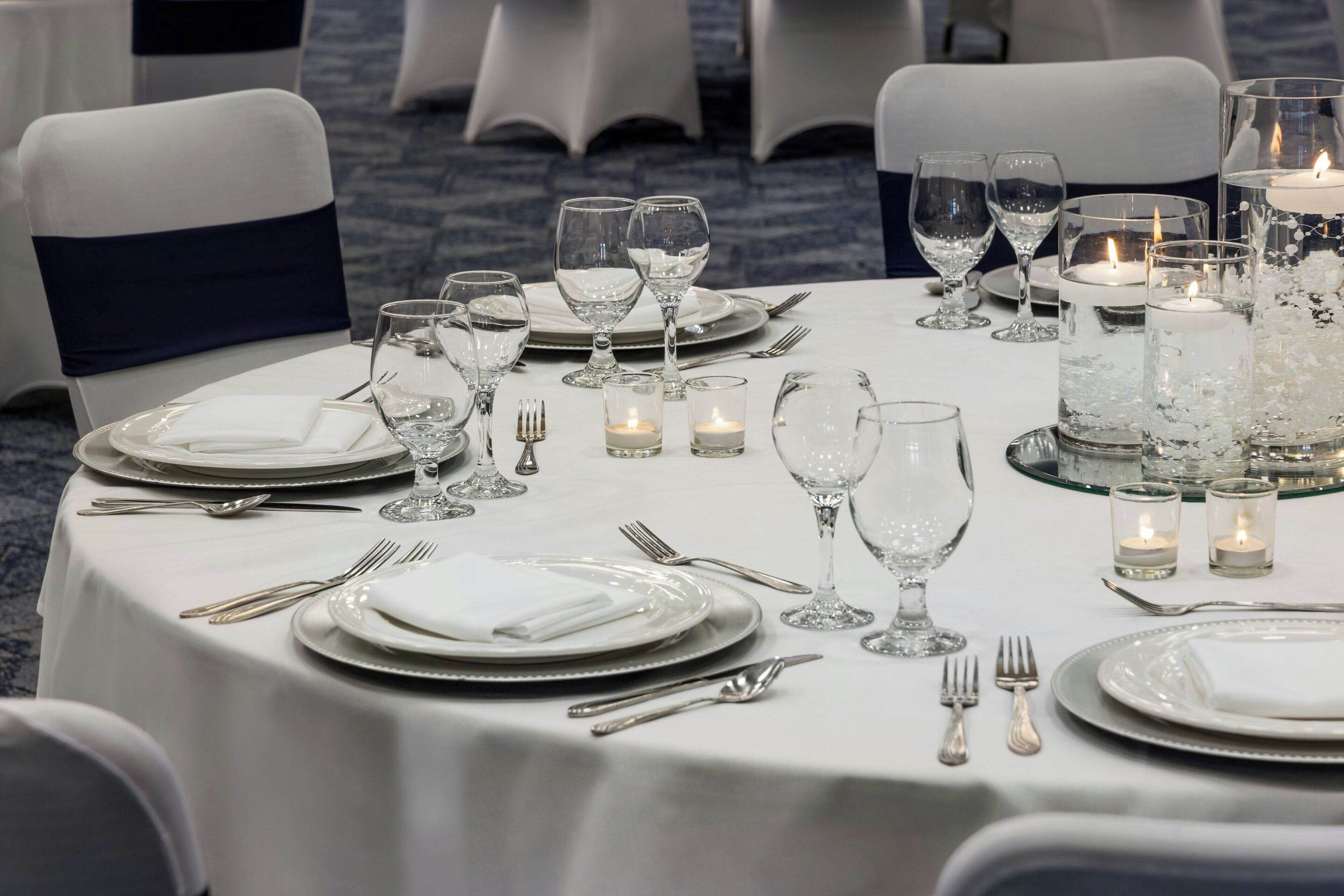 A formal dining table set with white tablecloth, plates, glasses, and candles.
