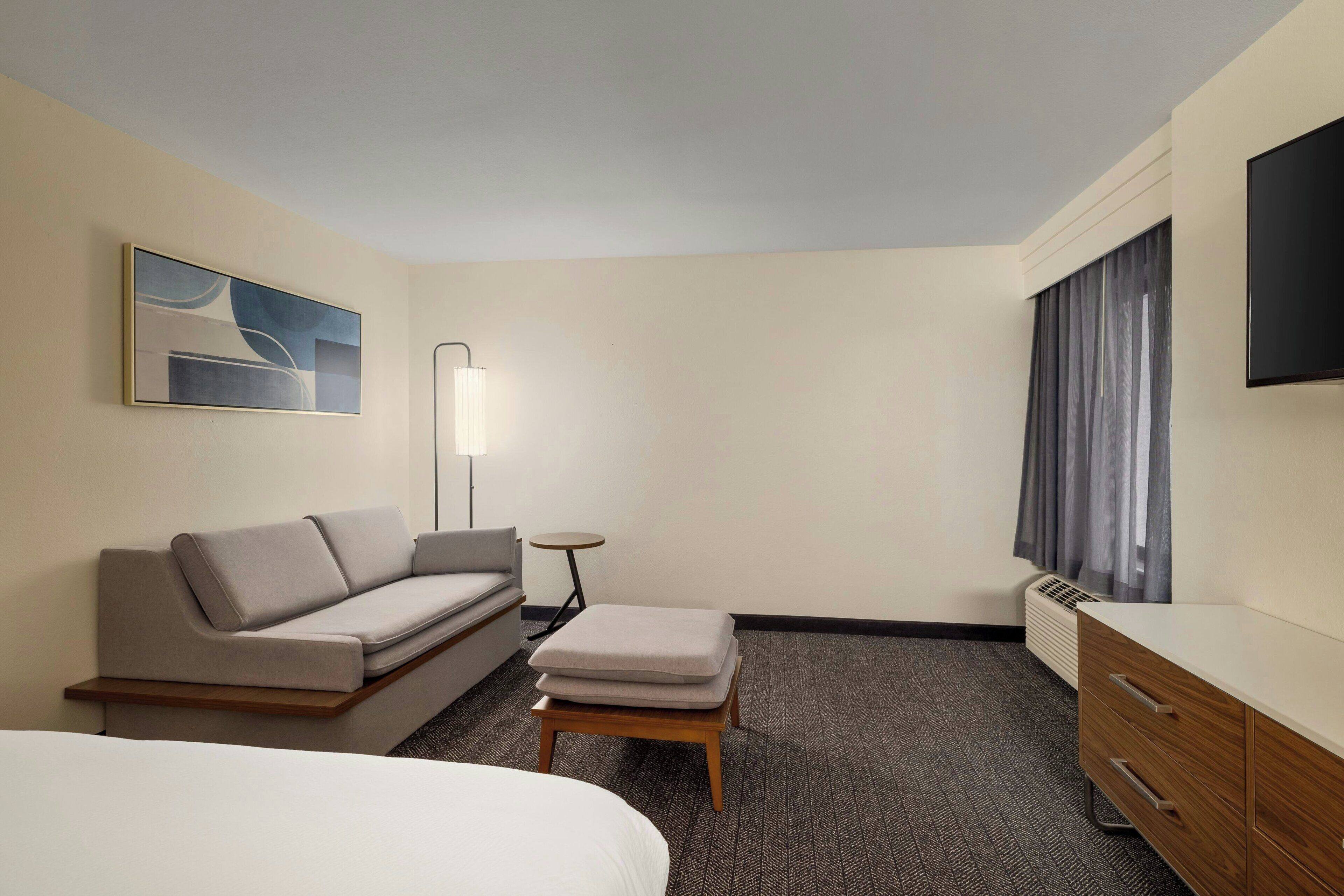 A hotel room with a bed, a sofa, a small table, a TV, and a window with curtains.