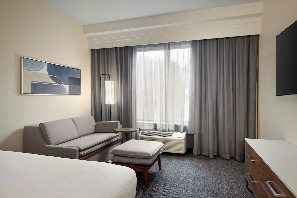 A hotel room with a bed, a sofa, a small table, a TV, and a window with curtains.