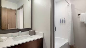 A modern bathroom with a double sink, a large mirror, a shower with a glass door, and toiletries on the wall.