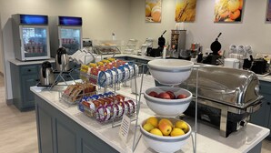 A buffet area with various food items, including fruits and packaged snacks, and a coffee station.