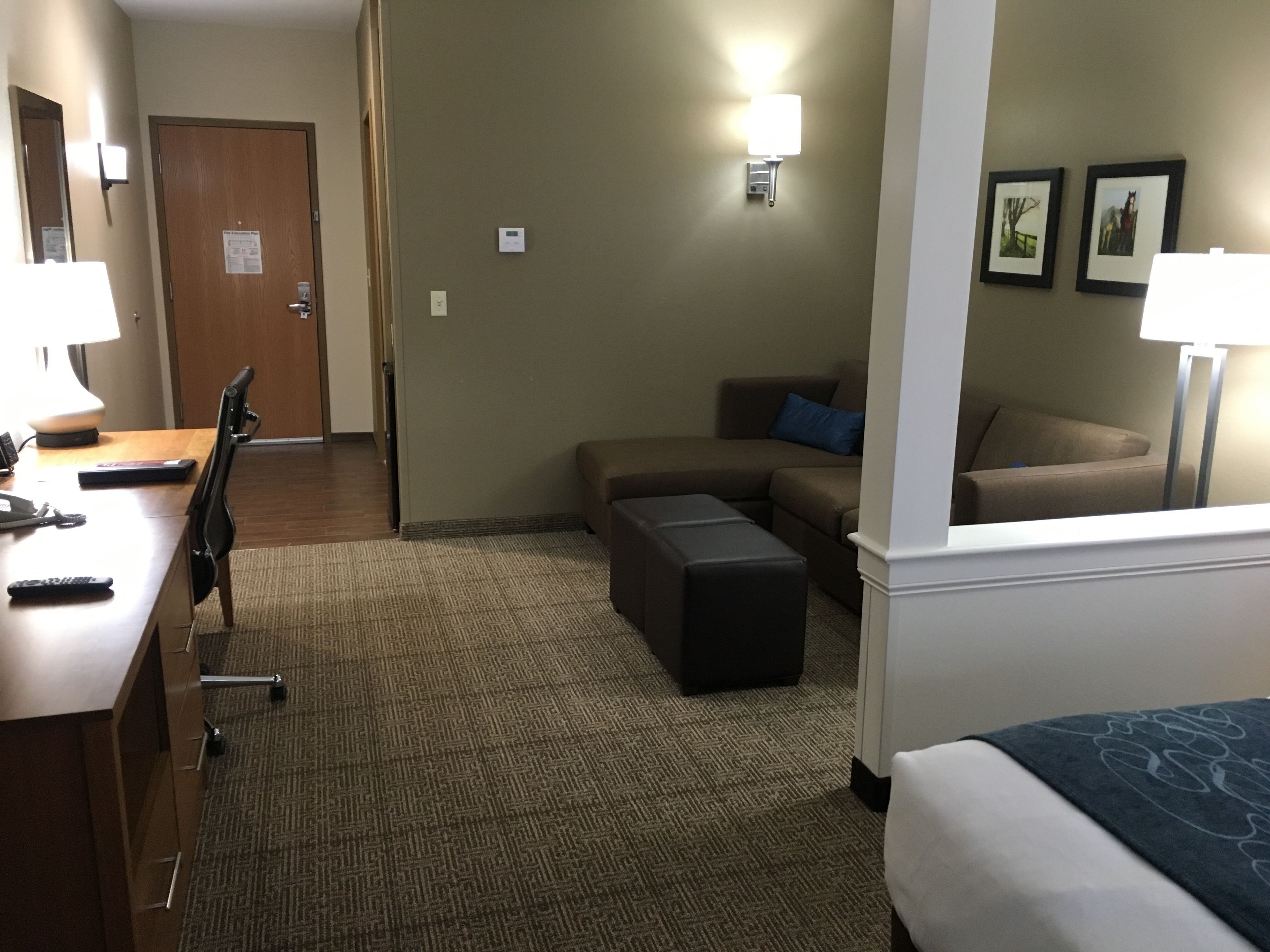 Una habitación de hotel con escritorio, silla, sofá, reposapiés y cama.