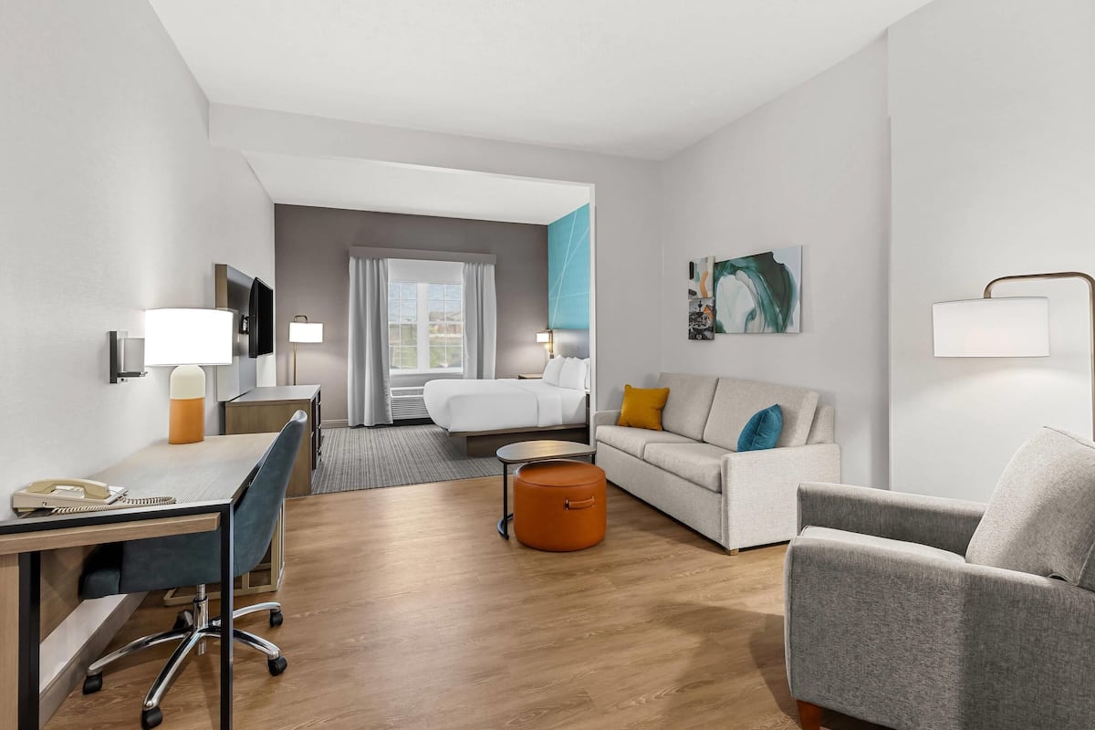 A modern hotel room with a desk, chair, sofa, and a bed.