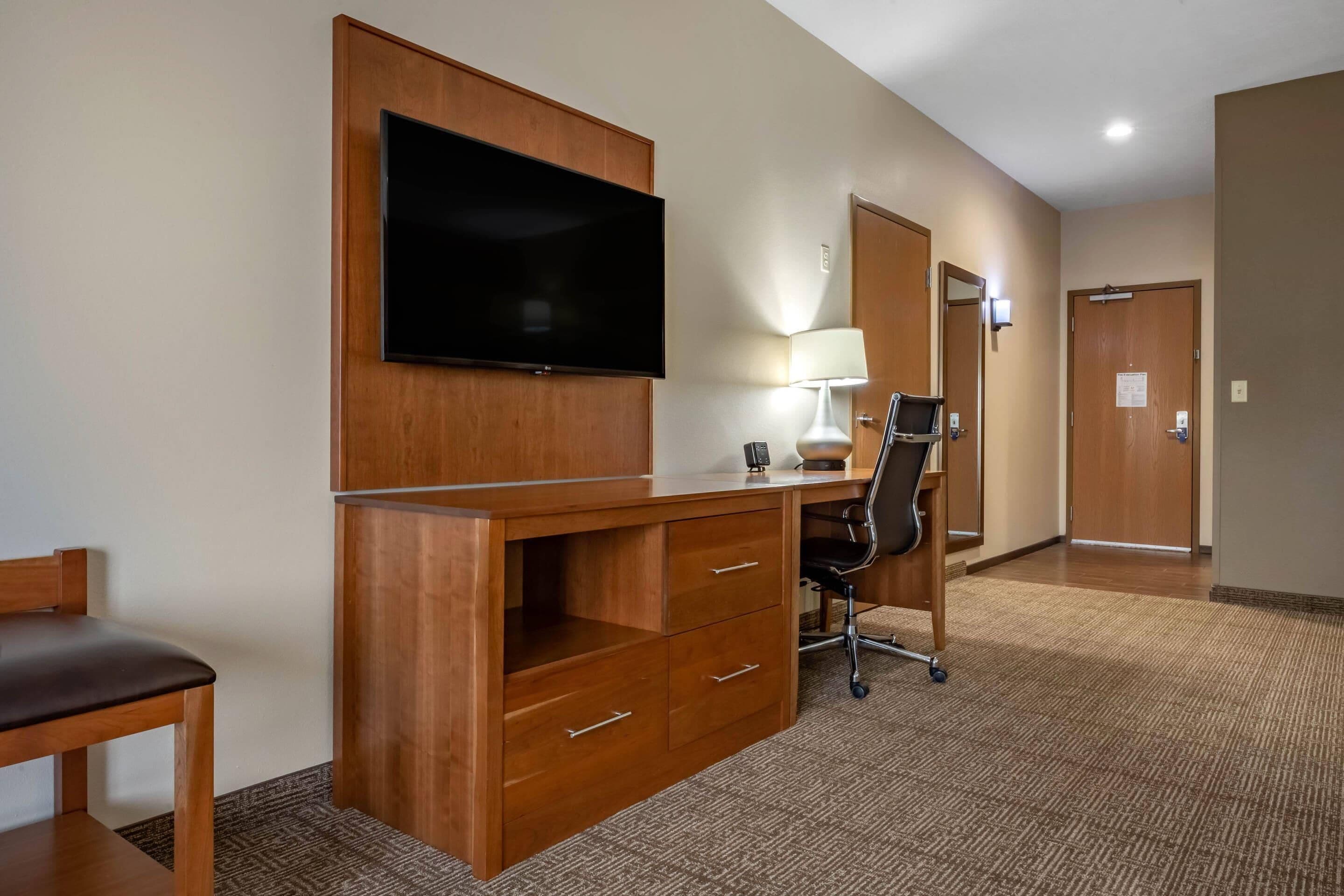 Habitación de hotel con escritorio de madera, televisor de pantalla plana, silla, lámpara de escritorio y puerta.