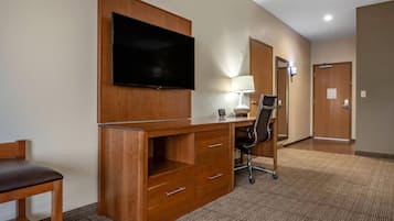 Habitación de hotel con escritorio de madera, televisor de pantalla plana, silla, lámpara de escritorio y puerta.