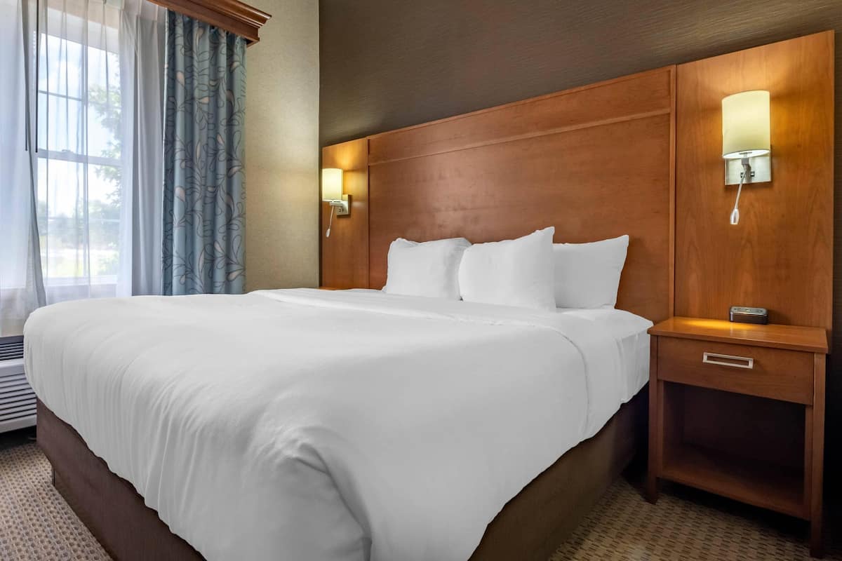 A hotel room with a large bed, wooden headboard, bedside lamps, and a window with curtains.