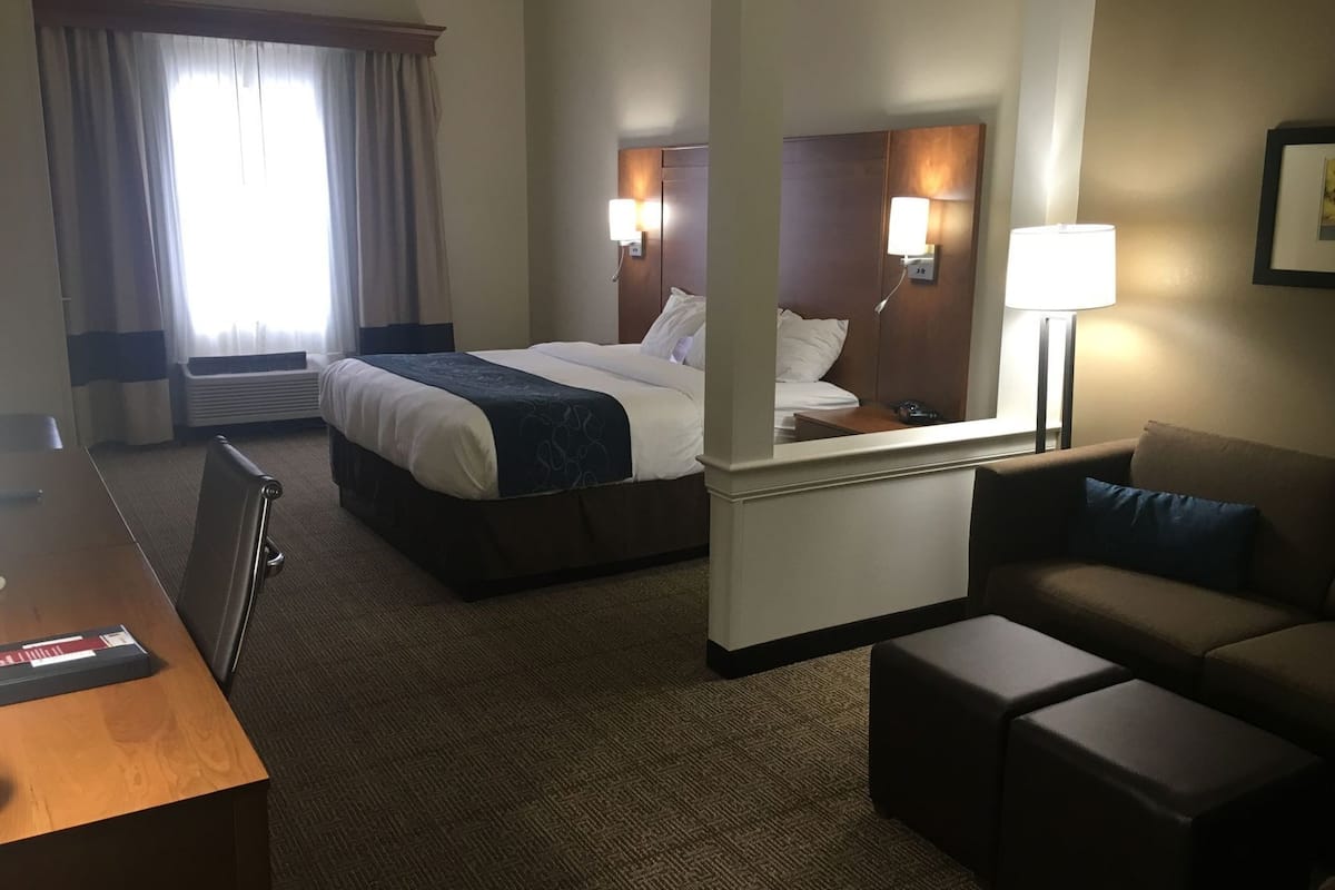A hotel room with a bed, a desk, a chair, a sofa, a lamp, and a window with curtains.