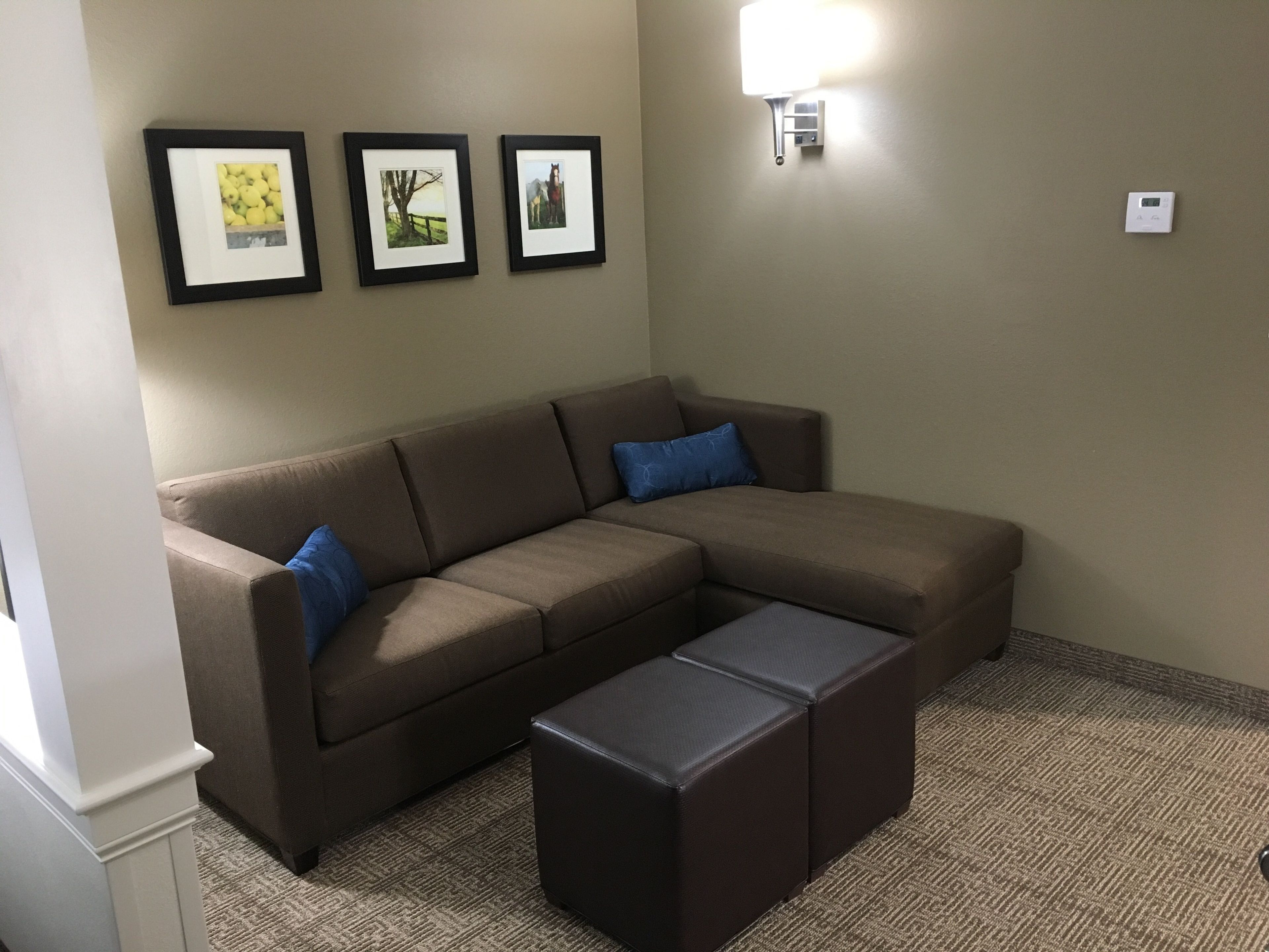 A living room with a brown sectional sofa, a small ottoman, and three framed pictures on the wall.